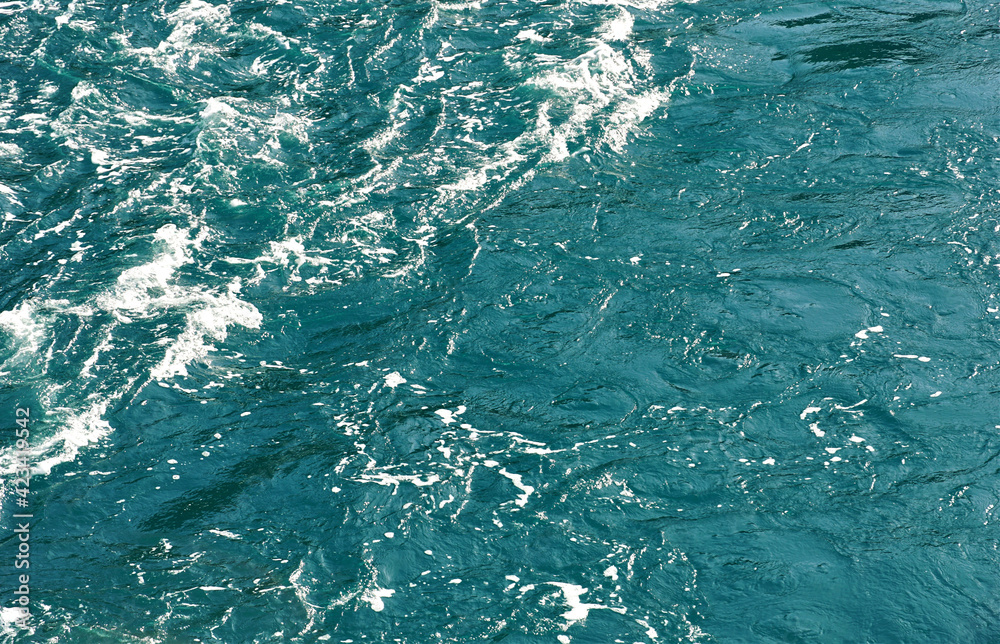 Emerald green color of rippled sea water surface with white foam on the top