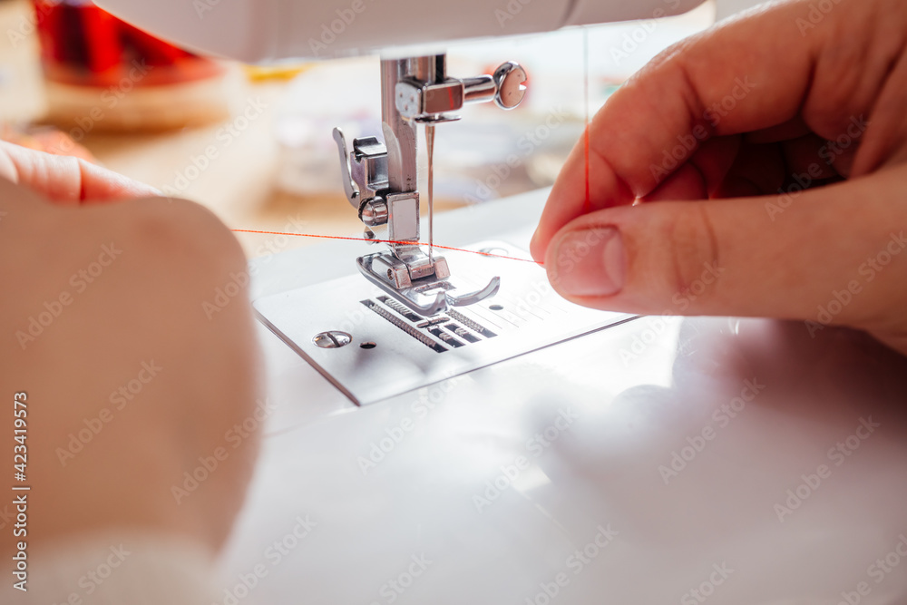 Closeup hands inserting thread into sewing machine needle