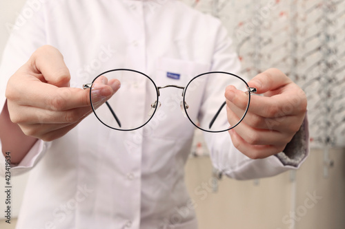 An optometrist in a white medical gown in an opticians salon holds round glasses for vision. Help in choosing eyeglasses. Eyesight check. Taking care of your health