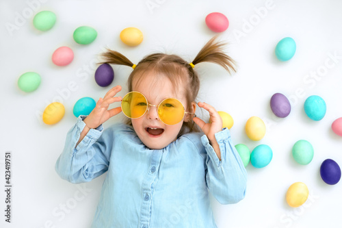 Portrait of a child in yellow sunglasses on a white background with Easter eggs