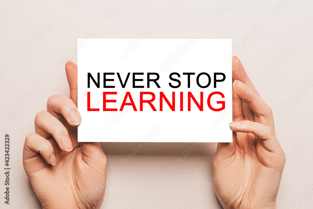 Female hands hold card paper with text Never Stop Learning on a yellow background. Education and study concept Female hands hold card paper with text Never Stop Learning on a yellow background. Education and study concept