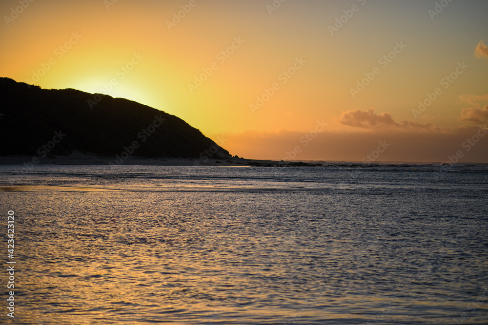 Landscape shot of ocean with sun protruding over hills