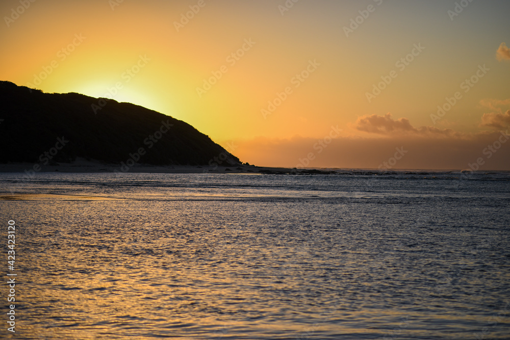 Landscape shot of ocean with sun protruding over hills Landscape shot of ocean with sun protruding over hills
