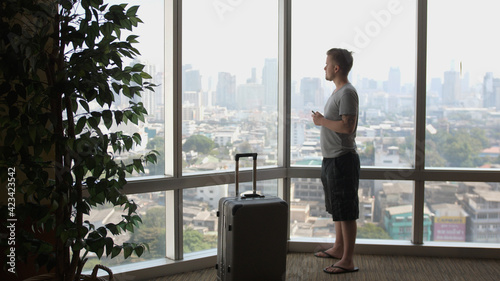 A man is enjoying smoking with wape in front of panoramic window with a luggage