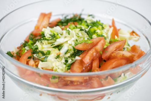 fresh salad with cabbage, tomatoes and greens in a glass bowl