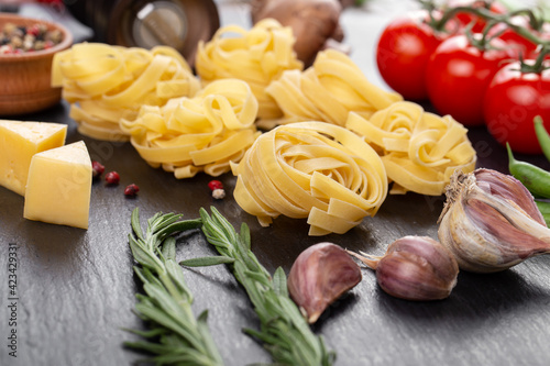 Raw pasta tagliatelle with fresh tomatoes, peppers, mushrooms,asparagus beans, spices and cheese on black table.