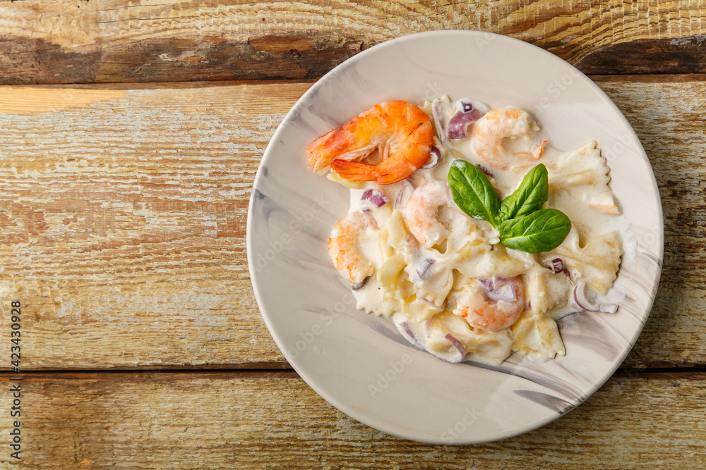 Pasta with shrimps in a creamy sauce, garnished with spinach on a gray plate on a wooden table Pasta with shrimps in a creamy sauce, garnished with spinach on a gray plate on a wooden table