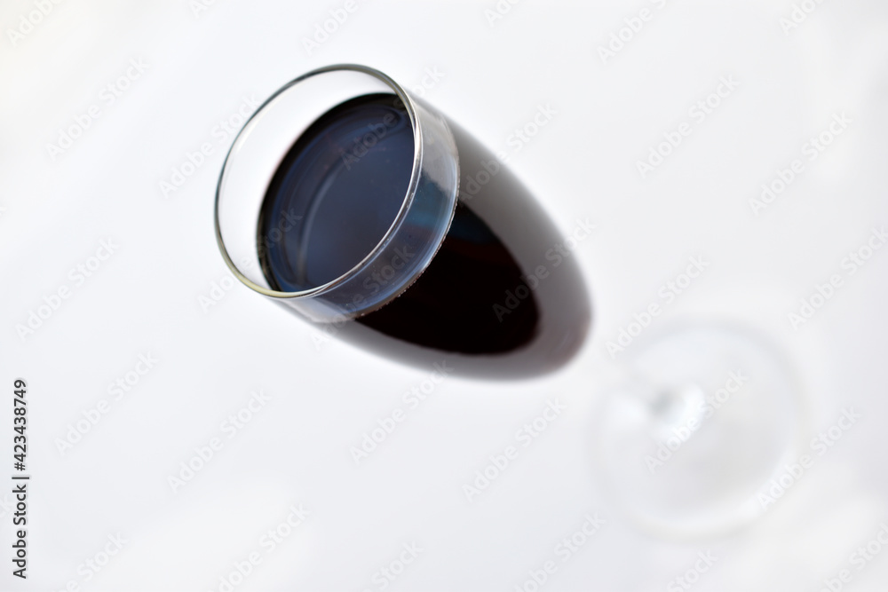 Small glass of red wine on a white background with shadows