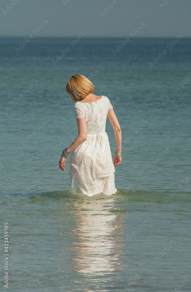 beautiful woman in sunglasses stands and poses in the sea in a white wedding dress beautiful woman in sunglasses stands and poses in the sea in a white wedding dress
