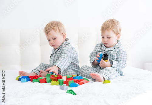 Two funny boys brothers twins on white bed in pajamas playing in constructor.