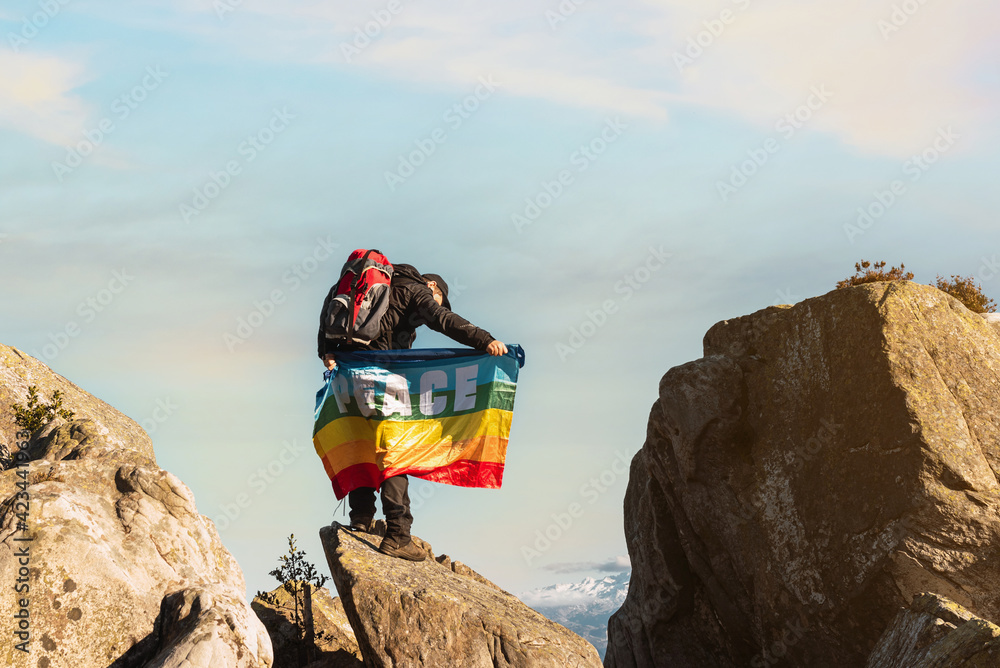 person holding a rainbow flag of peace on top of a mountain. hiker doing trekking. Mountain Sports.