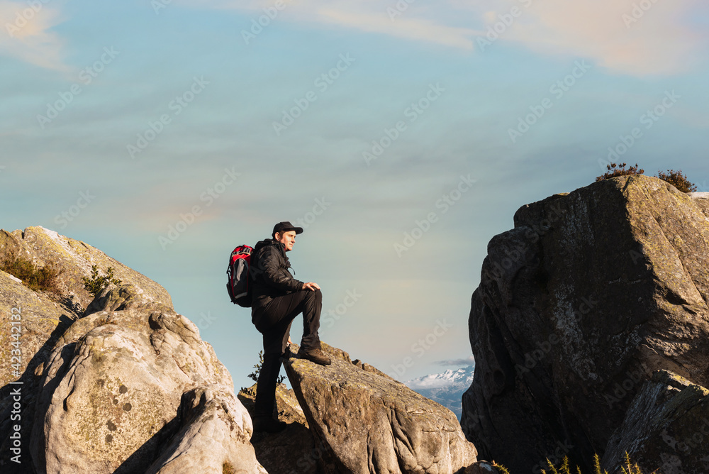 mountaineer posing on the rocks of a mountain at sunset. hiker contemplating the landscape weekend getaway. single person exercising. mountain activities.