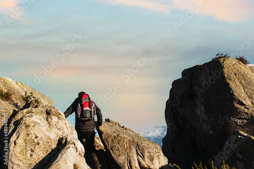 Unrecognizable hiker from behind with red backpack walking on the rocks of a mountain at sunset. mountain sports and activities. weekend getaway.