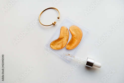 Gold eye patches, eye mask, gold particle serum and bracelet. Facial beauty and skin care concept.