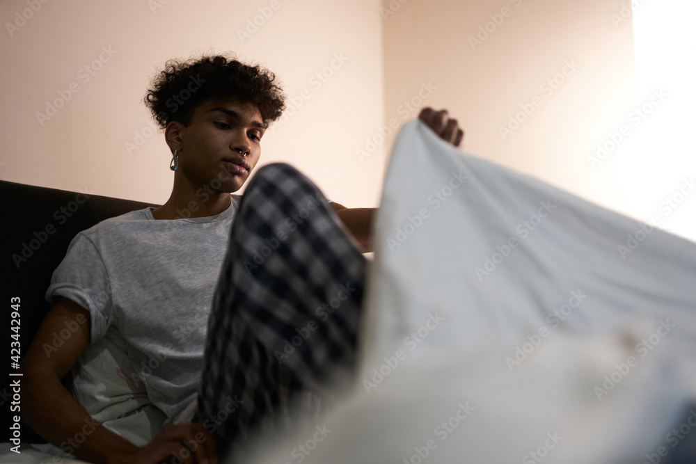 Relaxation. Young guy wearing pajamas going to bed covering