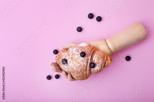 Wooden hand showing baked croissant with raw blueberriy on pink background photo