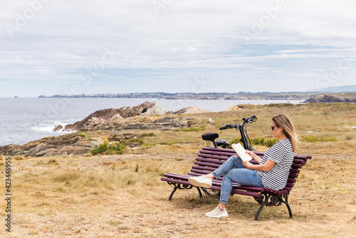 Woman sitting on a bench reading a book outdoor in front of the sea