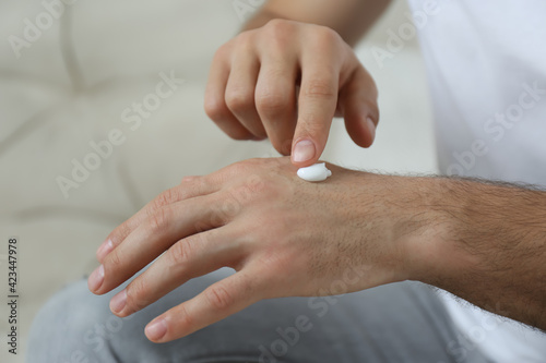 Man applying cream onto hand on sofa, closeup
