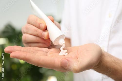 Man applying moisturizing cream from tube onto hand on blurred background, closeup