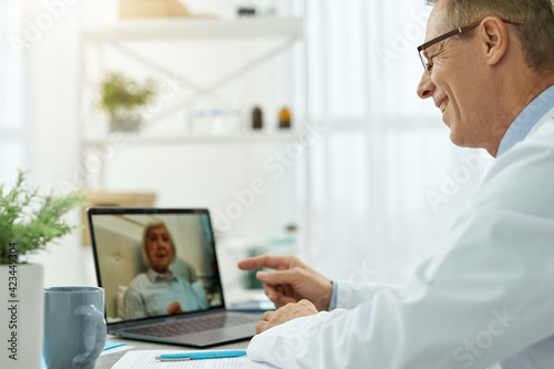 Cheerful doctor providing online consultation to old woman in clinic