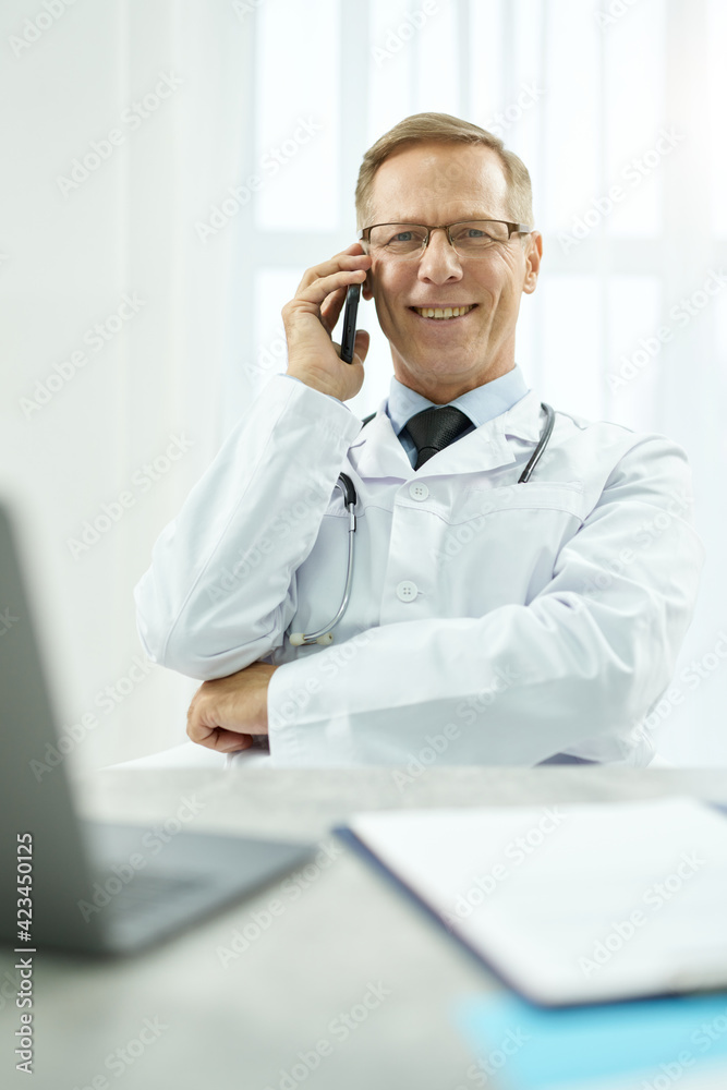 Cheerful male doctor talking on mobile phone at work
