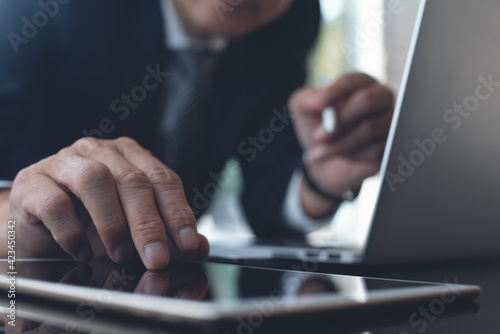 Close up of businessman finger touching on digital tablet and working on laptop computer at office