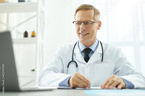 Cheerful male doctor using modern laptop at work
