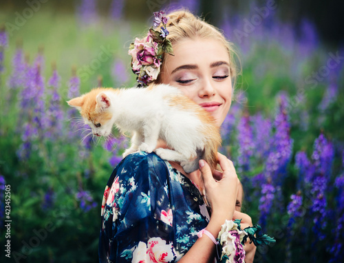 A small kitten is playing on the shoulder of a young beautiful girl in the summer nature