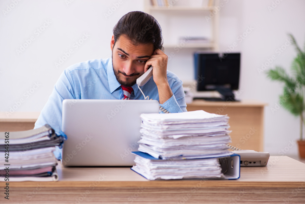 Young male employee unhappy with excessive work in the office Young male employee unhappy with excessive work in the office