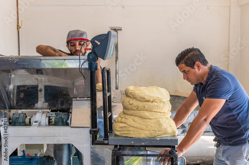 two young men working as a team to extract dough from a nixtamal mill photo