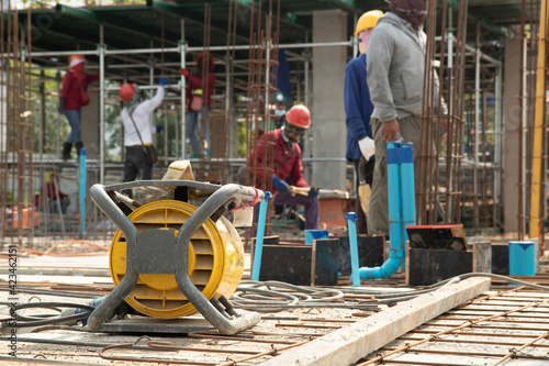Yellow concrete vibrater on rebar for floor pouring frame in construction area, background with columnar and building condition during construction.