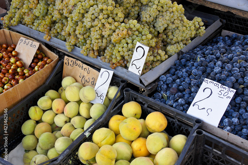 A variety of fresh fruit, including grapes, plums, and apricots, for sale at the Dezerters' Bazaar open-air market in Tbilisi, Georgia, with prices written in Georgian script photo