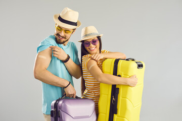 Happy family ready for safe summer vacation. Smiling young couple holding travel cases and showing arms after receiving modern Covid19 vaccine. Coronavirus vaccination concept