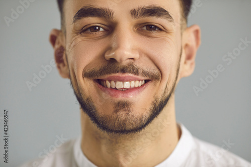 Closeup studio portrait of happy cheerful amiable young Caucasian man with stubble, friendly candid open smile and crow's feet wrinkles around his kind eyes. Human face, people's appearance concept