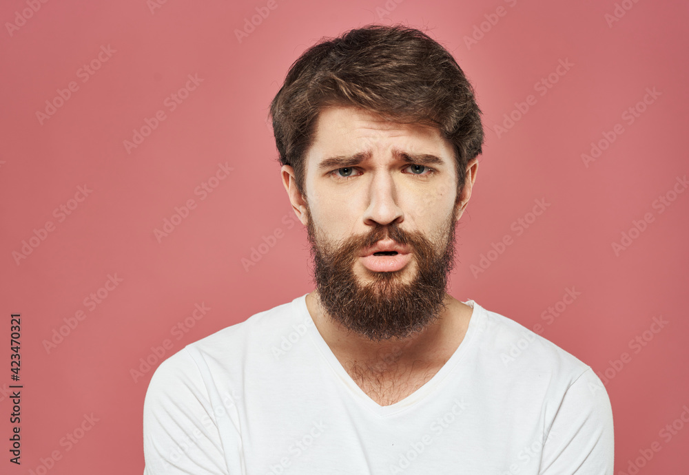 Portrait of an upset man in a white t-shirt on a pink background cropped view Portrait of an upset man in a white t-shirt on a pink background cropped view
