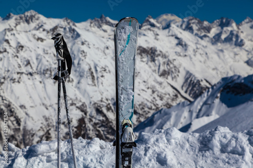 Skiing and ski poles stand vertically in the snow against the background of the ski descent