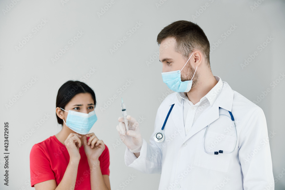 female patient in a medical mask looks at a syringe in the hands of a doctor covid 