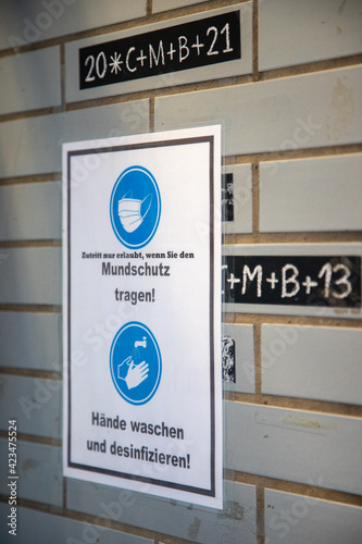 german sign on a wall at a shop entrance to wear mouth protection when entering the shop, because of corona virus. Sign is covering the blessing of Epiphany