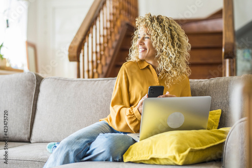 Smiling adult young woman sit relax on couch using modern laptop browsing unlimited wireless internet, happy young people freelancer work on computer typing texting from home, technology concept photo