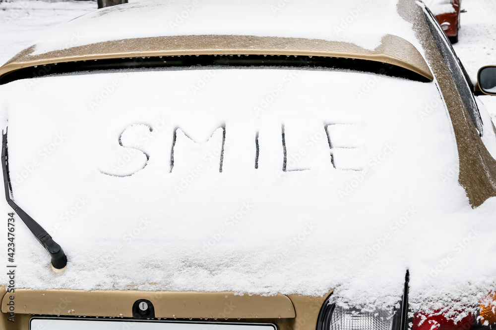 Word SMILE written on snow covered car window