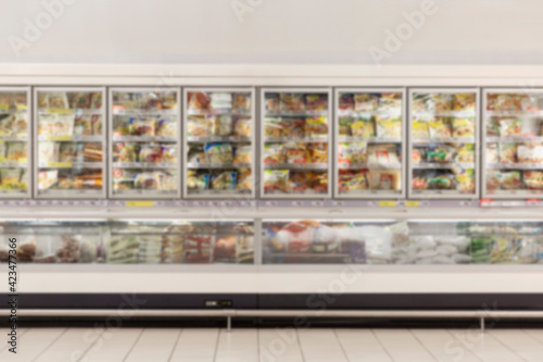 Glass display cases in the frozen food section of a supermarket. Front view. Blurred.