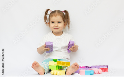 Adorable two year old girl playing with colorful plastic building blocks.