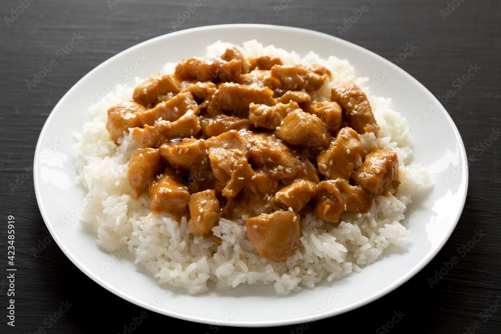Homemade Orange Chicken with White Rice on a white plate on a black background, low angle view. Close-up. Homemade Orange Chicken with White Rice on a white plate on a black background, low angle view. Close-up.