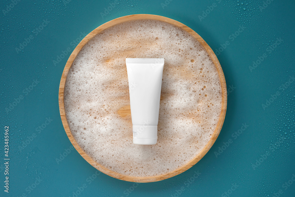 Stockfoto med beskrivningen Top view above of organic gentle facial  skincare product cleanser white tube with soap water bubbles and blank  label on bamboo light brown wooden plate colorful solid plain grey