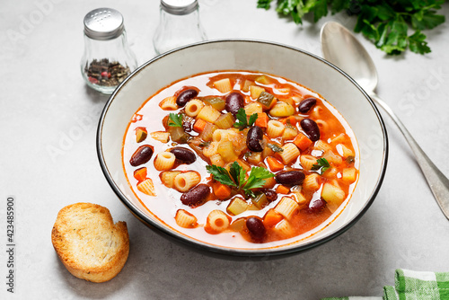 Vegetarian minestrone italian soup made with fresh vegetables, pasta and beans. Light gray background.
