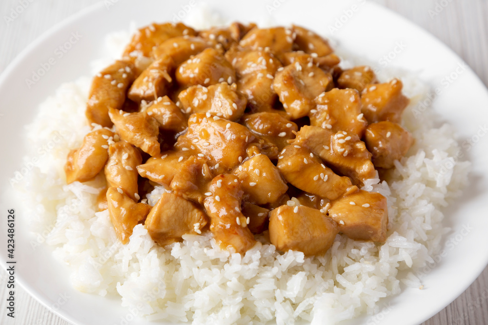 Homemade Orange Chicken with White Rice on a white plate on a white wooden background, side view. Close-up. Homemade Orange Chicken with White Rice on a white plate on a white wooden background, side view. Close-up.