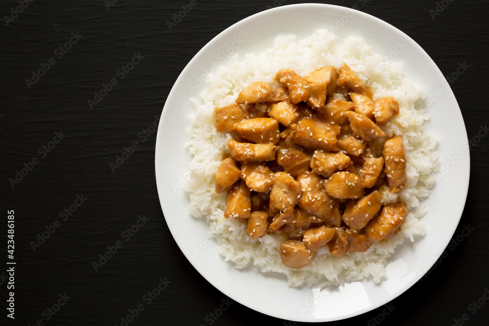 Homemade Orange Chicken with White Rice on a white plate on a black background, top view. Overhead, from above, flat lay. Copy space. Homemade Orange Chicken with White Rice on a white plate on a black background, top view. Overhead, from above, flat lay. Copy space.
