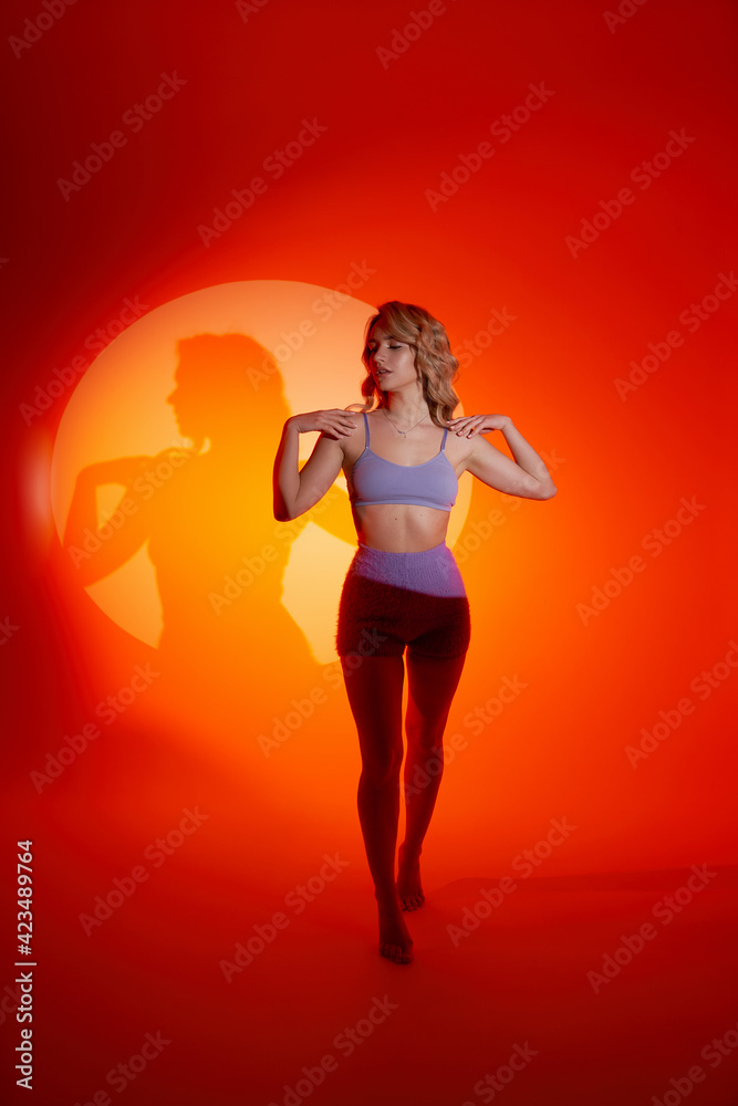 Young tanned woman with curly hairstyle posing in purple swimsuit, imitation of the sun with light