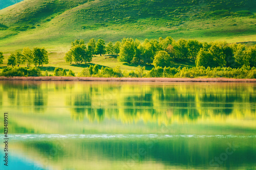 Green trees on the mountains and their reflections in the lake. Beautiful summer landscape. South Ural, Russia