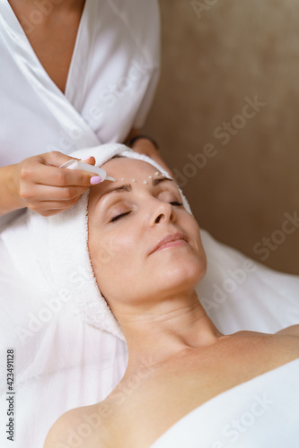 Face and Eye cream treatment or therapy. Dermatologist applying lotion on female skin